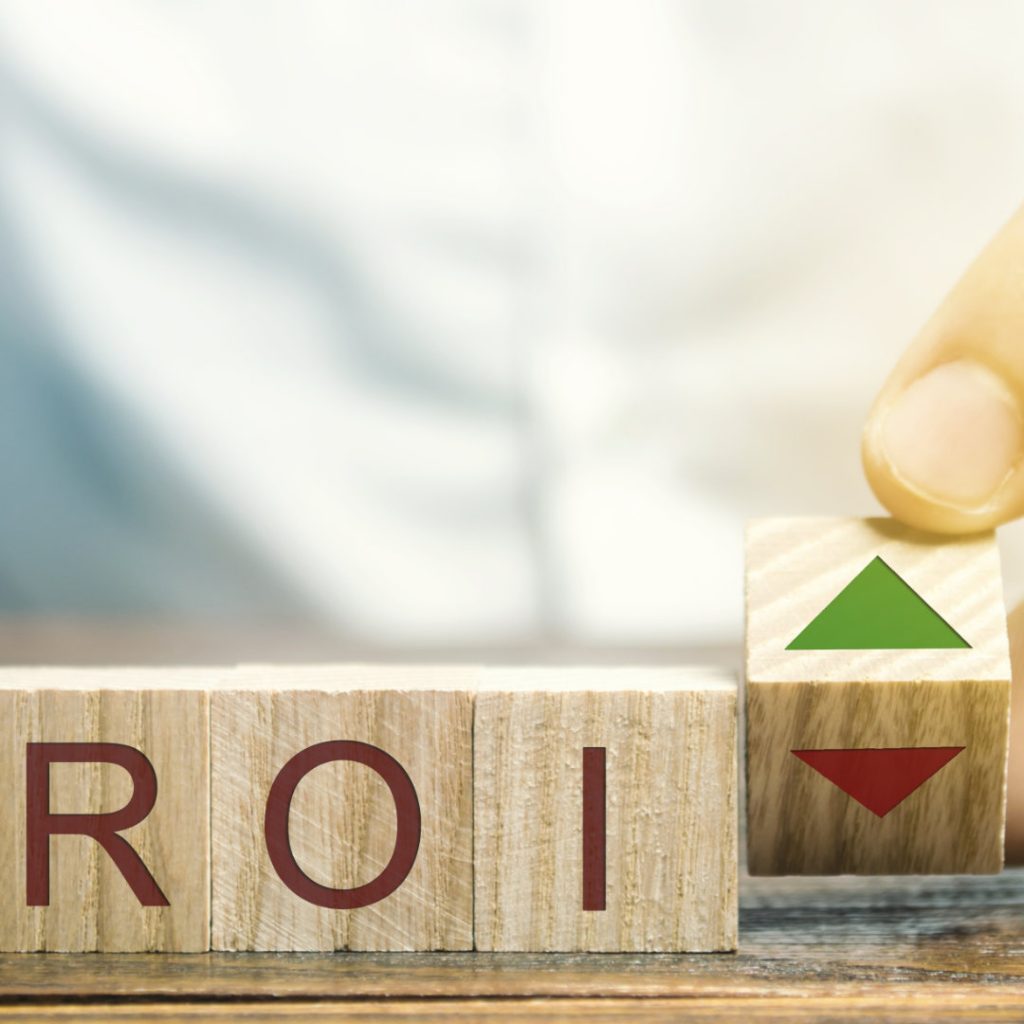 Wooden blocks with the word ROI and green arrow up. High level of business profitability. Return on investment, invested capital, rate. Success. Growth. Analytics. Report